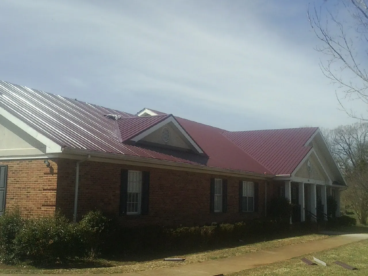 Red metal roof with gabled entries on a long brick building, from a Hail Damage Roof Repair job in Davis